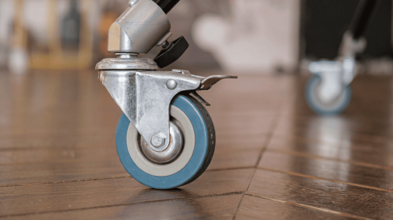 Close-up of a blue rubber caster wheel with a swivel bracket and locking brake on a wooden floor.