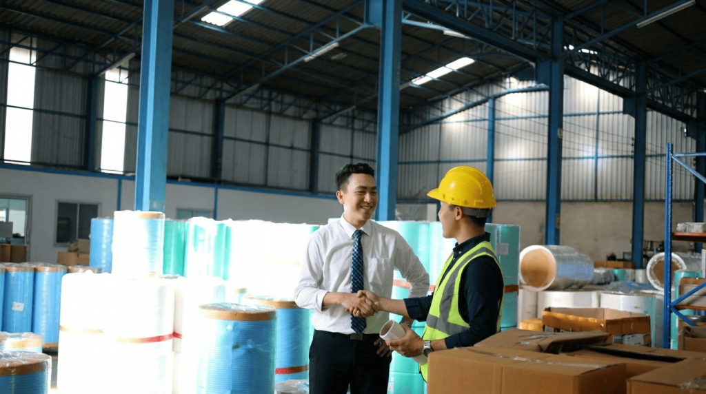 Business owner and engineer shaking hands inside an industrial facility