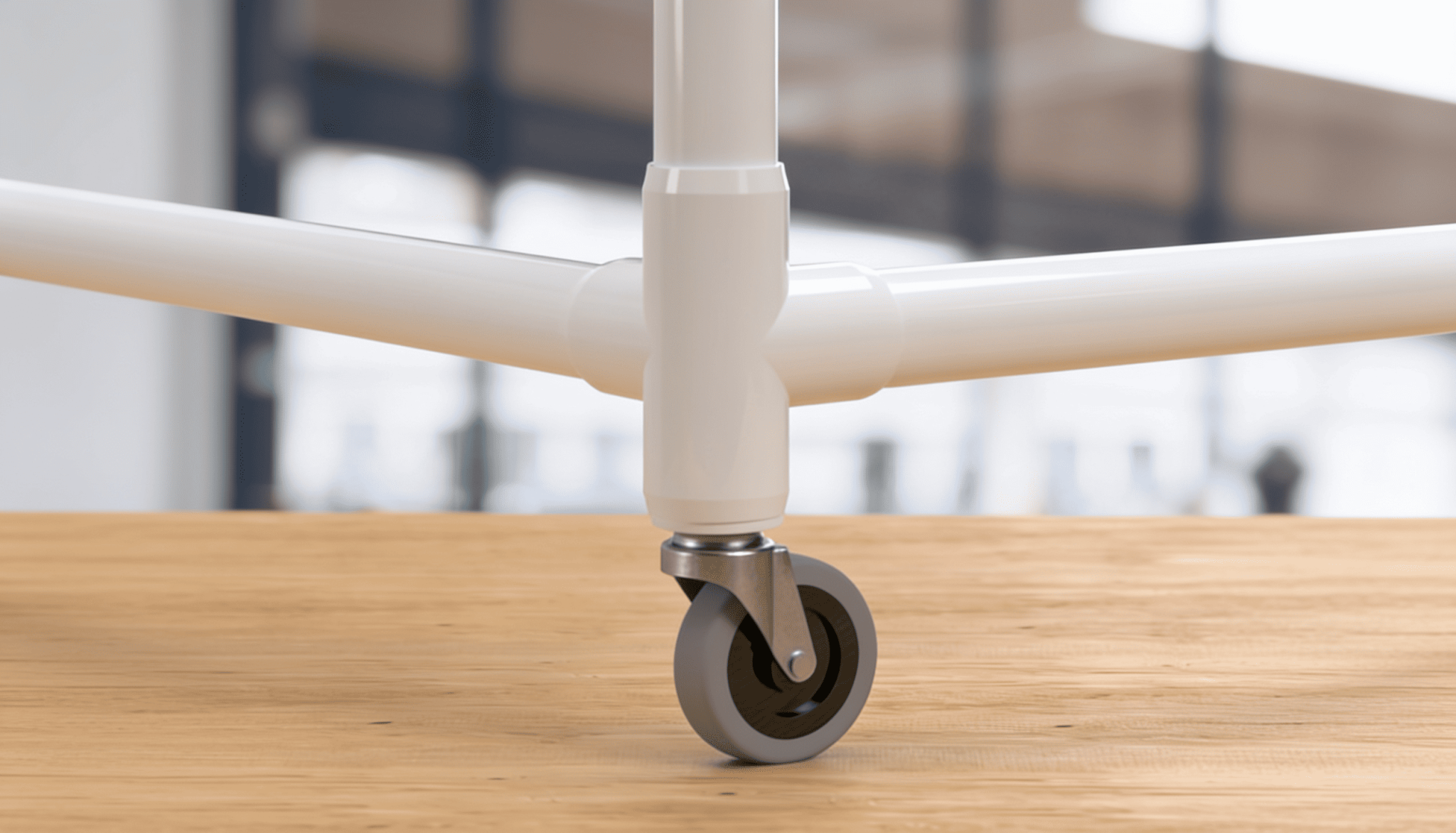 Close-up of a PVC swivel caster wheel attached to a white tubular pipe frame on a wooden floor
