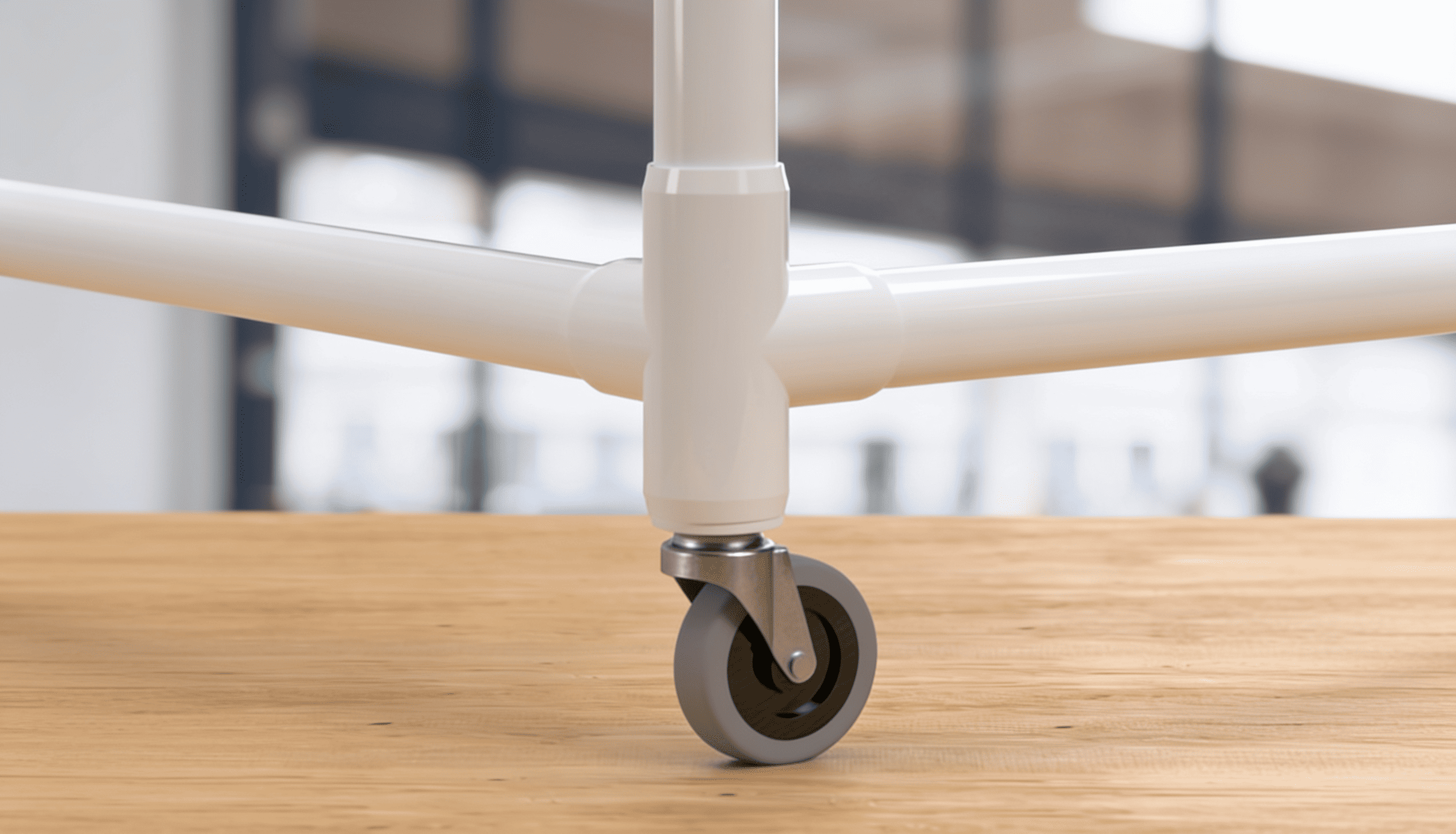 Close-up of a PVC swivel caster wheel attached to a white tubular pipe frame on a wooden floor