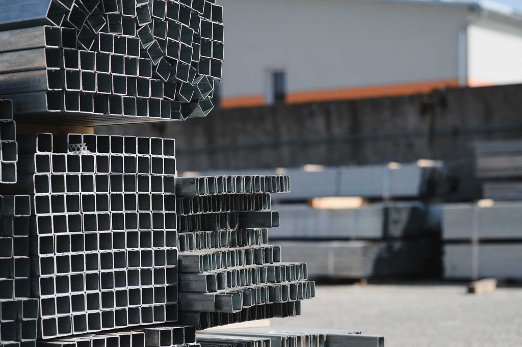 Large outdoor stack of hollow square steel tubes and structural metal profiles ready for construction